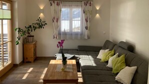 A living room with a sofa, a coffee table, a potted plant, and a window with curtains. - Holiday Home 'Bei Schönwetter' with Mountain View, Private Terrace & Wi-Fi (Bleiberg)