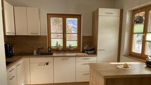 A modern kitchen with a central island, wooden cabinets, a built-in oven, and a window with a view of trees. - Holiday Home 'Bei Schönwetter' with Mountain View, Private Terrace & Wi-Fi (Bleiberg)