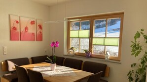 A dining area with a wooden table and chairs, a potted orchid, and a window with a view of a snowy landscape. - Holiday Home 'Bei Schönwetter' with Mountain View, Private Terrace & Wi-Fi (Bleiberg)