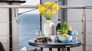 Un tavolo da balcone con un vaso di fiori gialli, bottiglie di birra, bicchieri e una ciotola di snack.