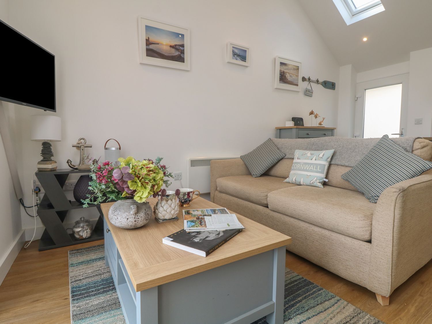 A cozy living room with a sofa, a coffee table, and a TV. There are framed pictures on the wall and a skylight above the sofa.