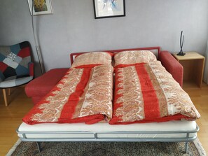 Un lit recouvert d’une couvre-lit à motifs, une chaise au design géométrique et une petite table avec une lampe.