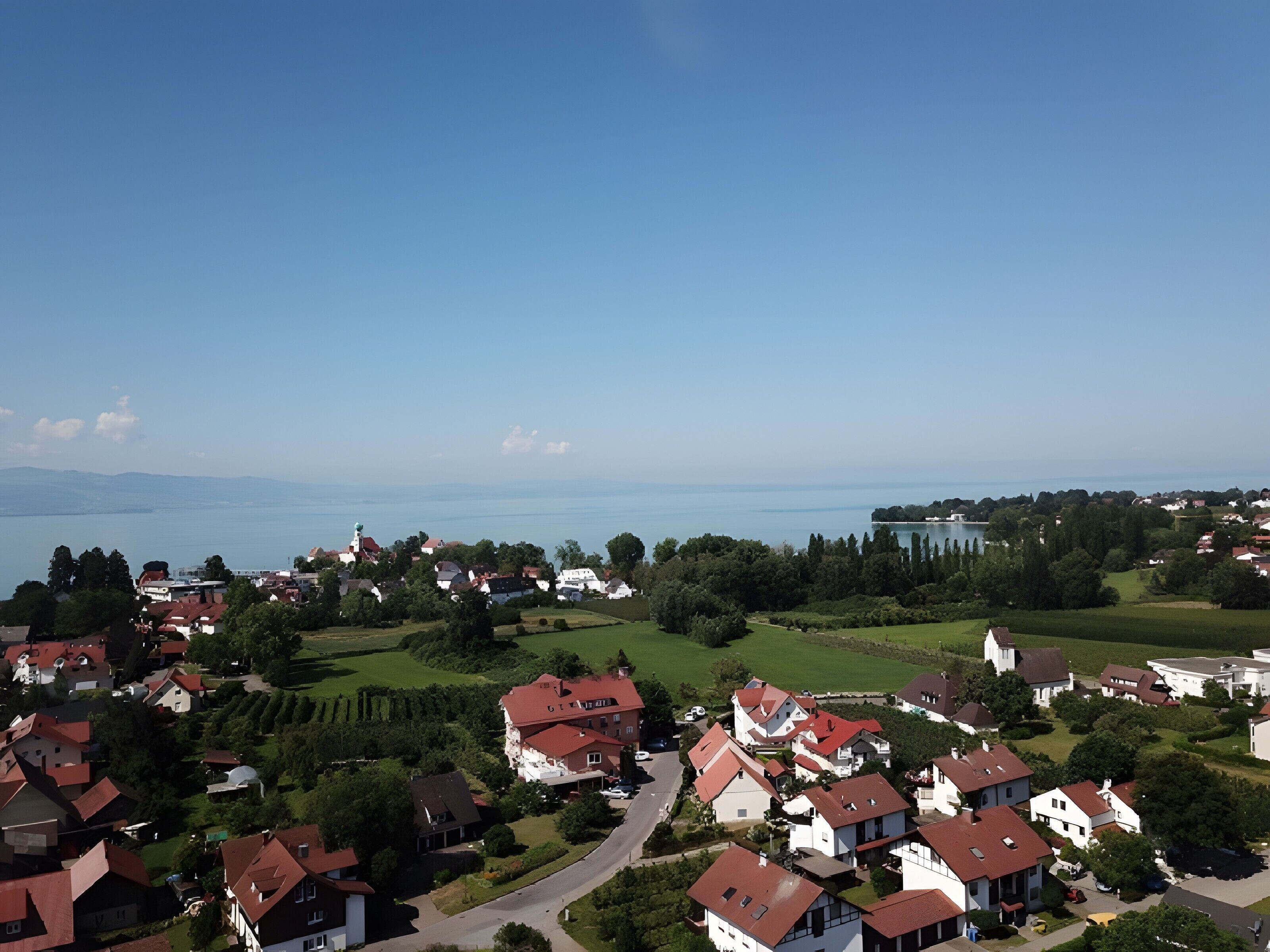 A residential area with houses, a road, and a body of water in the background.