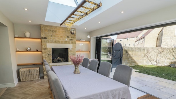 A dining area with a long table, chairs, a fireplace, and a view of the outside. - 2 Summers Way (Moreton-in-Marsh)