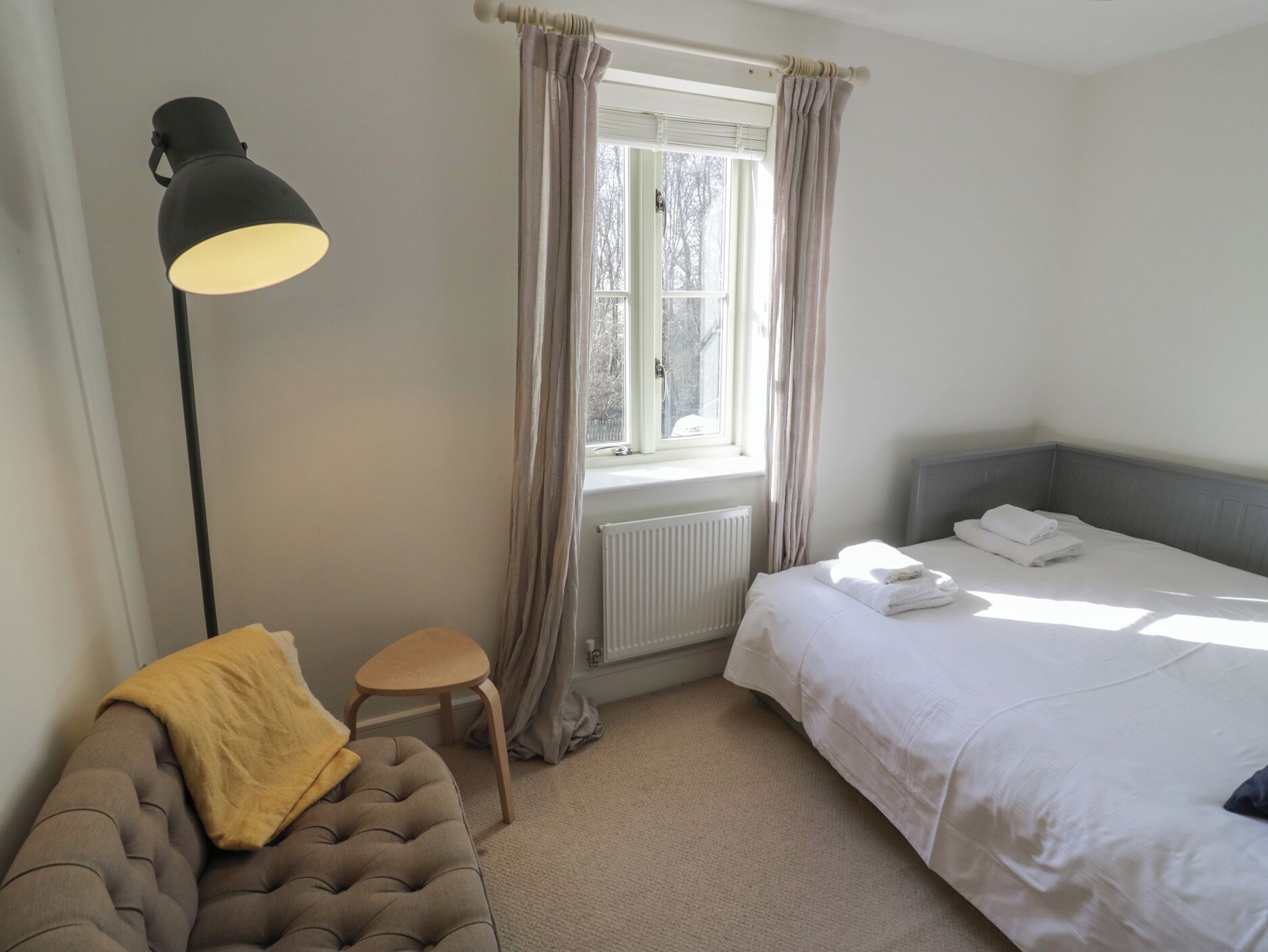 A bedroom with a bed, a bedside table, a lamp, and a window with curtains.
