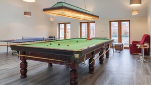 Egy biliárdasztal egy olyan helyiségben, ahol tetőablakok vannak, egy piros szék és egy pingpongasztal is található.