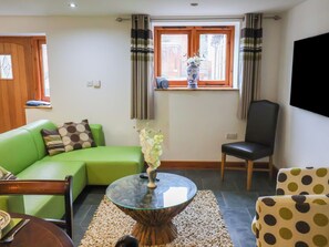 A living room with a green sofa, a round glass coffee table, a black chair, and a window with curtains. - Lime Cottage (Exeter)