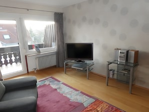 A living room with a sofa, a flat-screen TV, a glass coffee table, and a patterned rug.