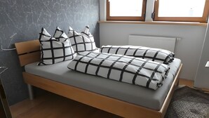 A bed with a checkered bedspread and pillows, a wooden headboard, a radiator, and a window with a view. - Apartment 'Diepold' with Mountain View, Shared Garden and Wi-Fi (Wasserburg (Bodensee))
