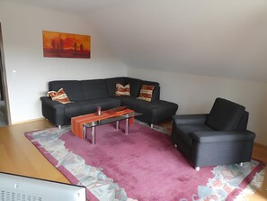 A modern living room with a black sofa, a glass coffee table, and a patterned rug.