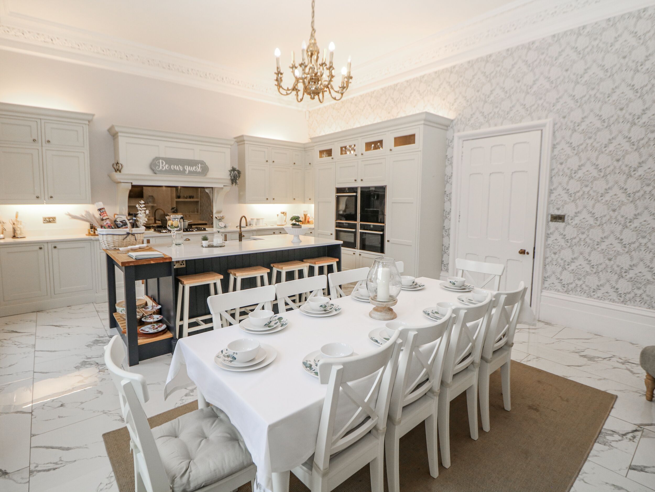 Una cocina amplia con muebles blancos, una isla central con taburetes y una zona de comedor preparada para seis comensales.