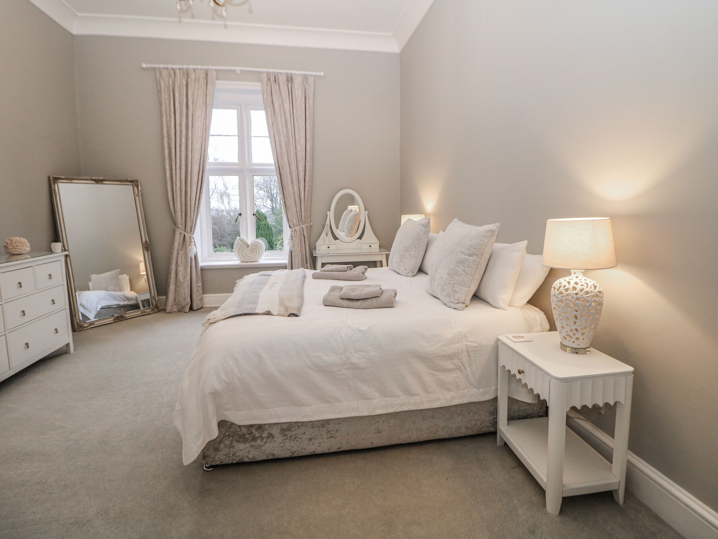 A bedroom with a bed, a dresser, a mirror, a lamp, and a window with curtains.