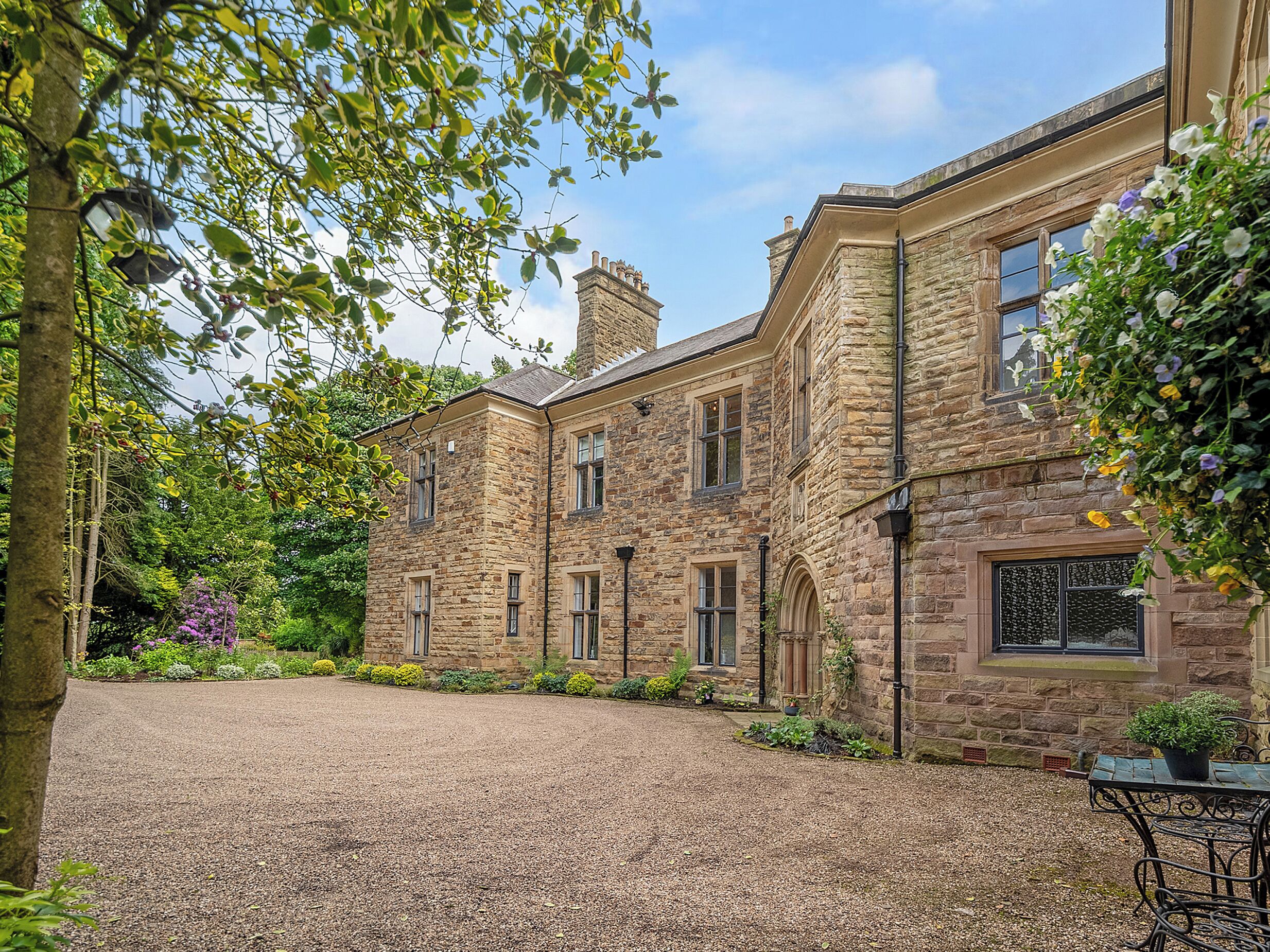 A stone building with a gravel driveway and a garden with various plants and flowers.