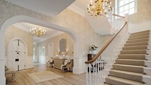Un vestíbulo espacioso con una imponente escalera, piso de madera y elegantes candelabros.