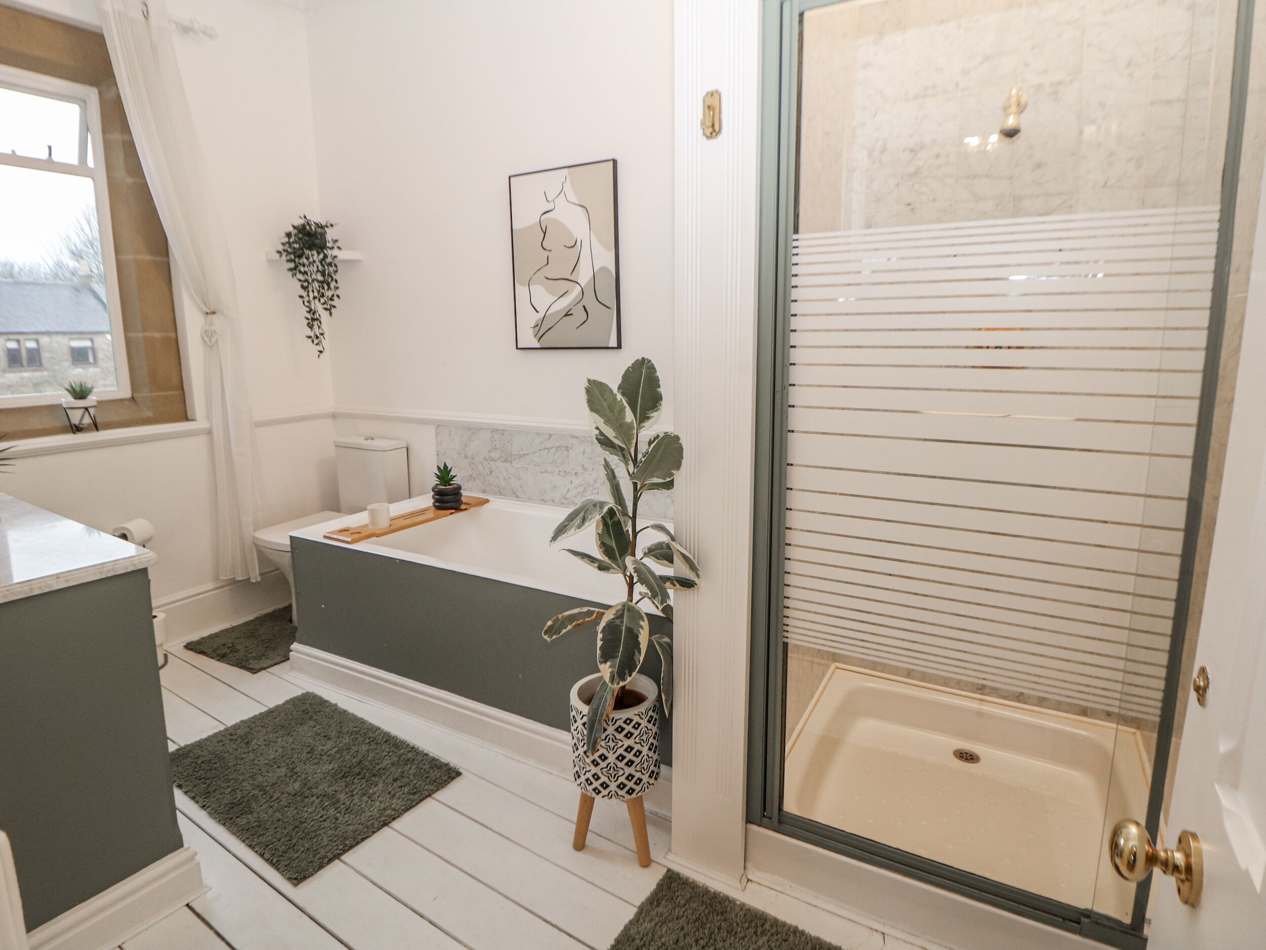 Un baño moderno con bañera, ducha e inodoro. Hay una planta pequeña en el suelo y un cuadro en la pared.