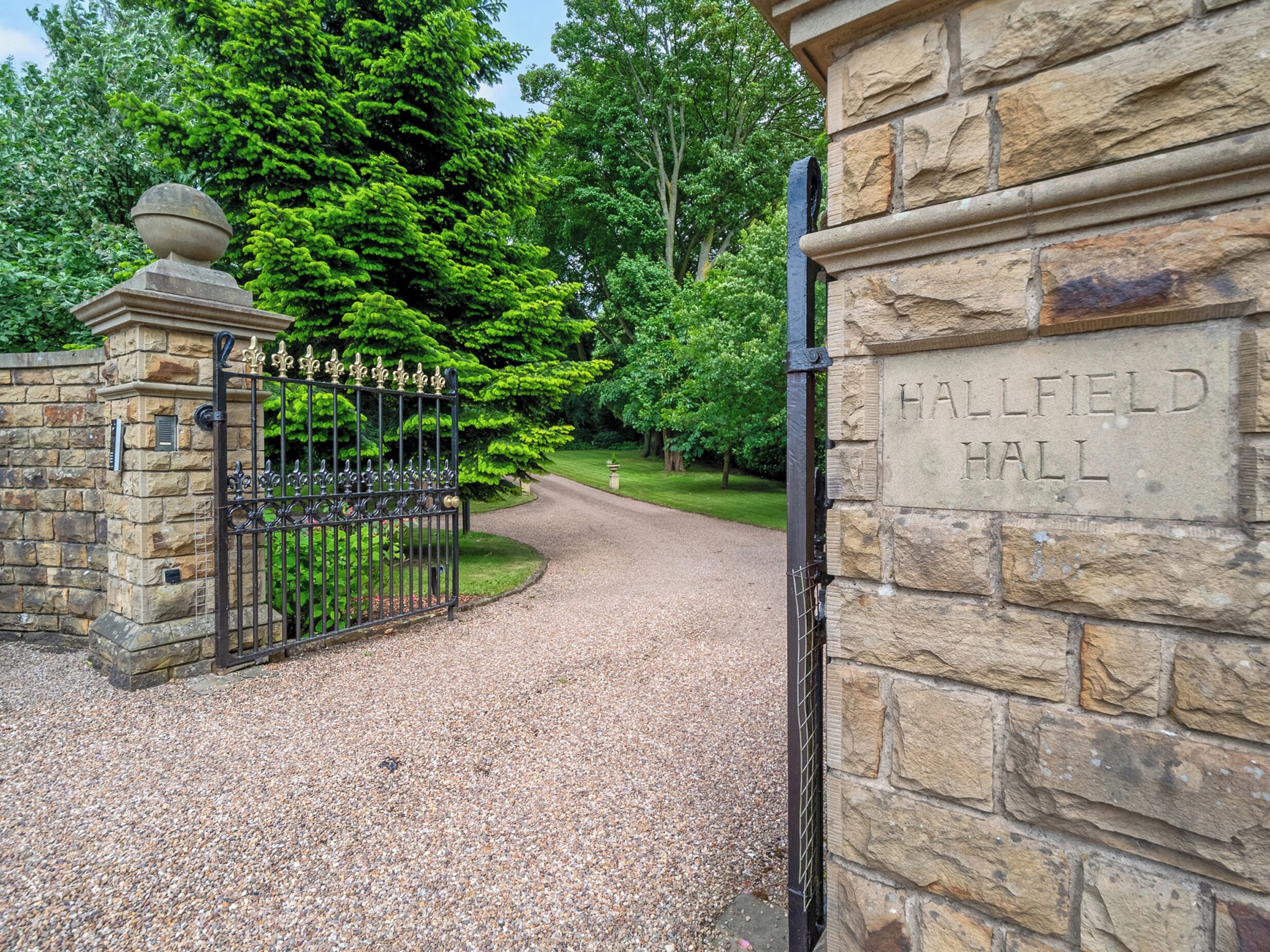 Un cancello in pietra con una recinzione in metallo e un cartello che riporta la scritta "HALFIELD HALL".