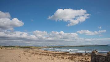 A beach with a stone wall, a few people, and a building in the distance.