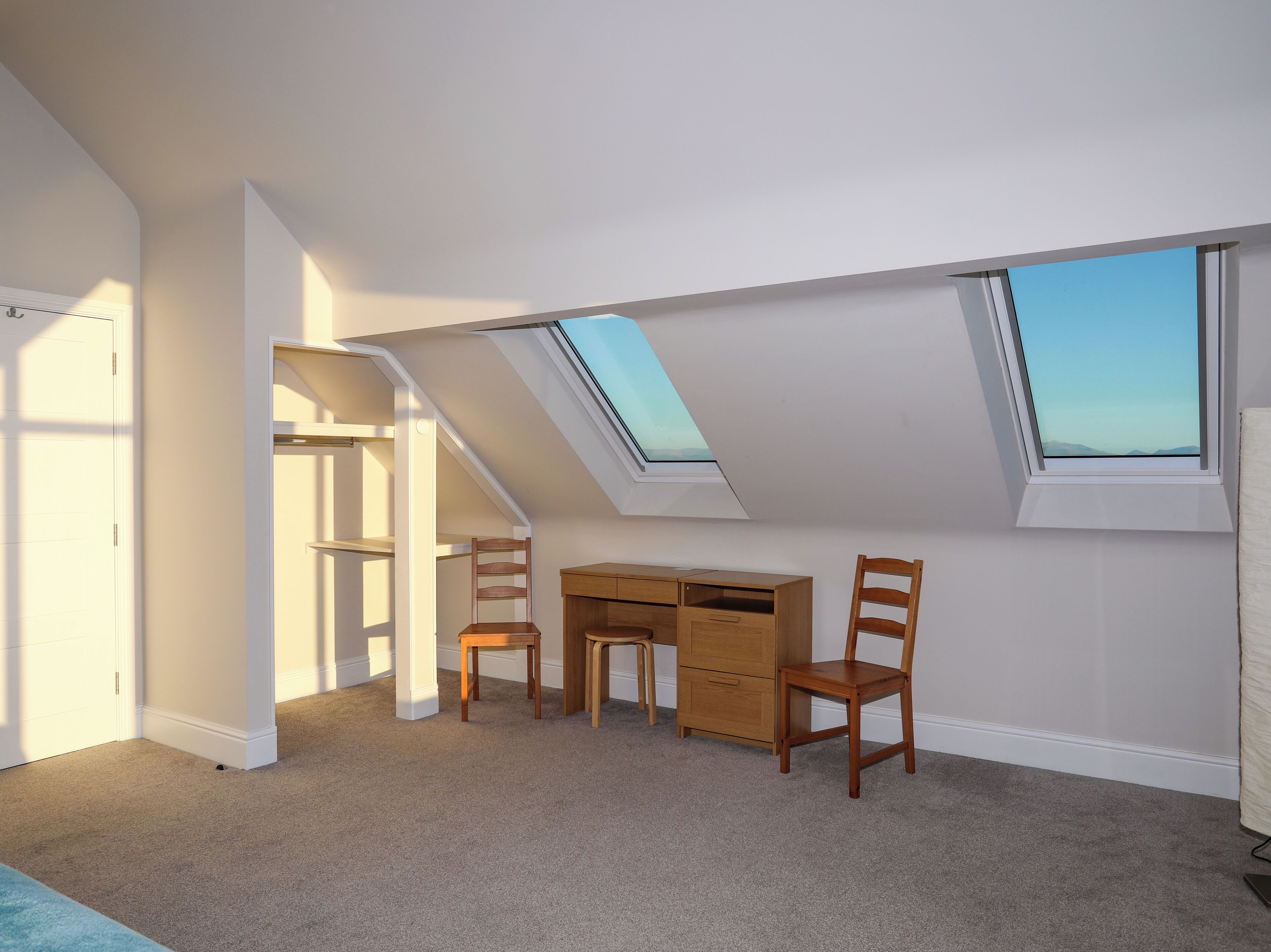 A room with a sloped ceiling, skylights, a desk, two chairs, and a carpeted floor.