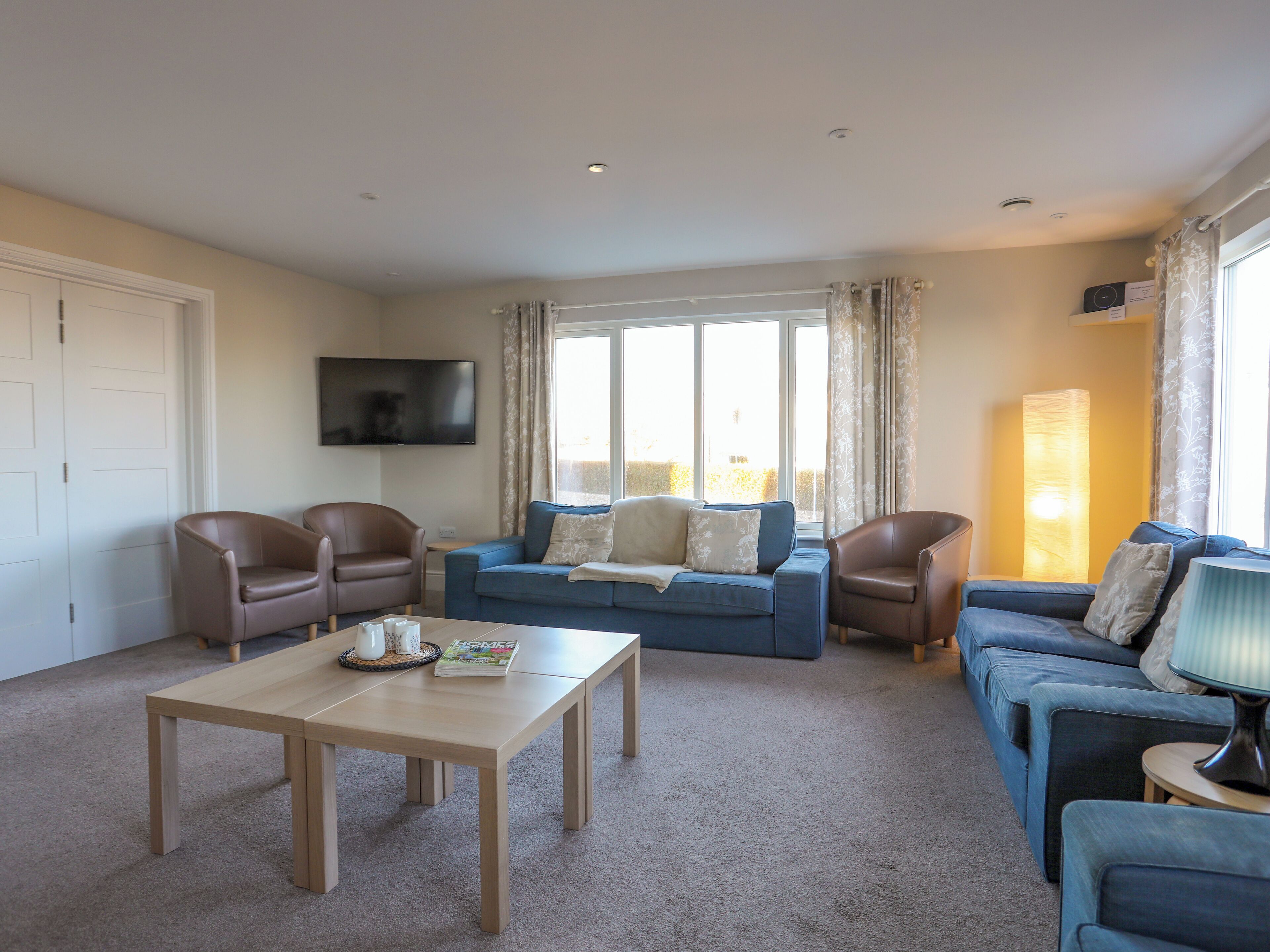 A living room with a sofa, two armchairs, a coffee table, and a TV mounted on the wall.