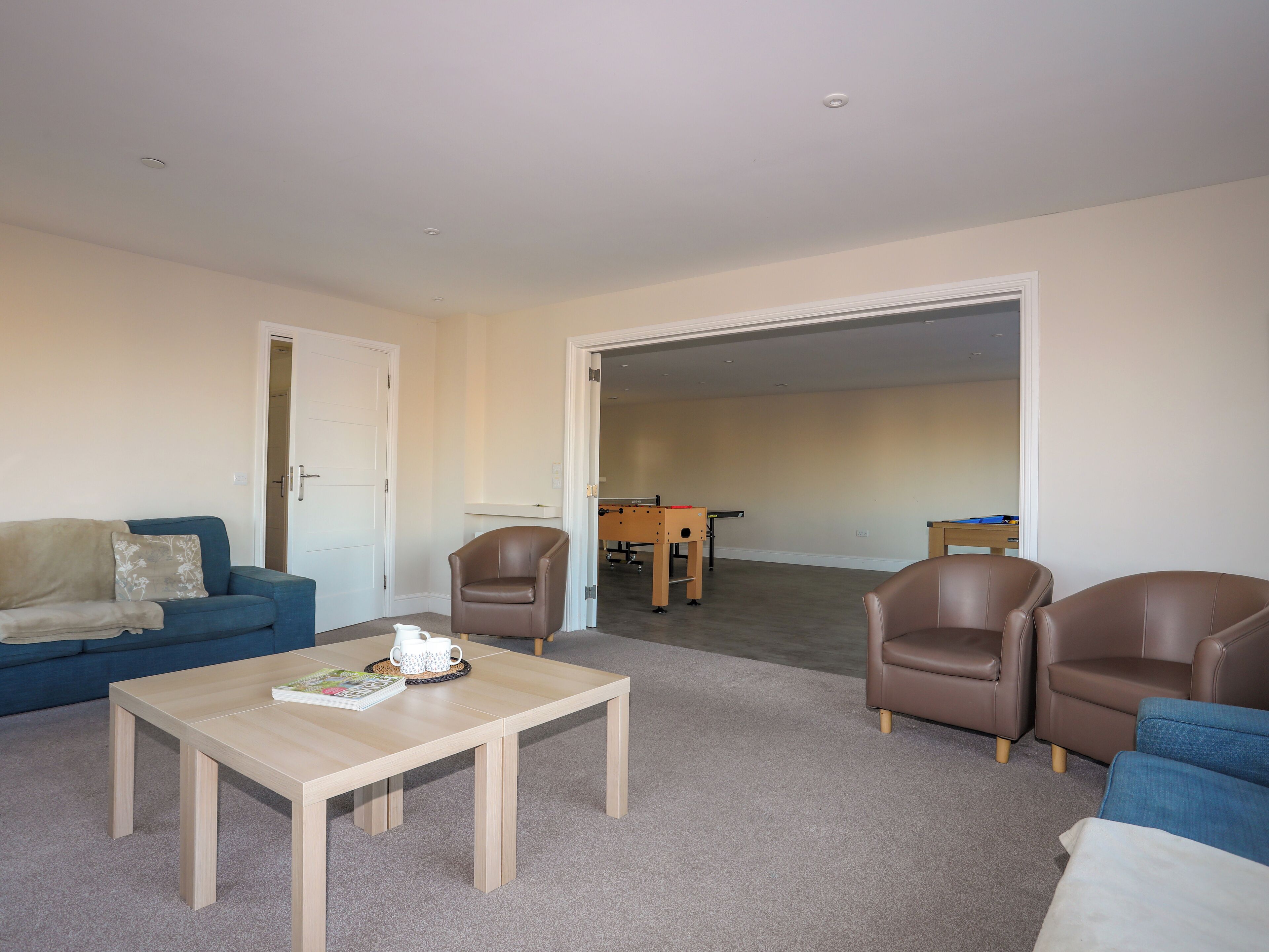 A living room with a sofa, two armchairs, a coffee table, and a door leading to another room.