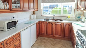 Una cocina con armarios de madera, microondas, lavabo y ventana con vistas a casas.