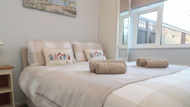 Una cama bien hecha con colcha a cuadros, dos almohadas con diseño costero y toallas enrolladas sobre la cama.