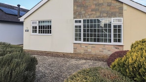 Una casa de dos pisos con fachada de piedra y exterior blanco. Tiene una ventana pequeña en la planta baja y una ventana más grande en el piso superior.