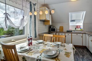 Ett kök med ett matbord för fyra personer, en mikrovågsugn och ett fönster med gardiner.