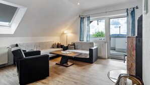 Un salon moderne avec un canapé, des fauteuils, une table basse, une lampe et une vue sur l’extérieur.
