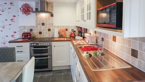 A modern kitchen with white cabinets, a stainless steel sink, and a red microwave. - Poppy Cottage (Exeter)