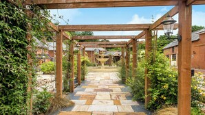 A stone pathway leading through a wooden pergola structure with a lantern on the right.
