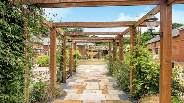 A stone pathway leading through a wooden pergola structure with a lantern on the right. - Poppy Cottage (Exeter)