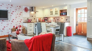 A modern kitchen with white cabinets, a microwave, and a dining area with chairs and a table. - Poppy Cottage (Exeter)
