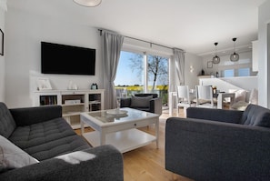 Un salon moderne doté d’un téléviseur à écran plat, de canapés gris, d’une table basse et offrant une vue sur l’extérieur.