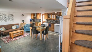 Een moderne keuken met houten kastjes, een eethoek met een tafel en stoelen, en een woonkamer met een bank en salontafel.