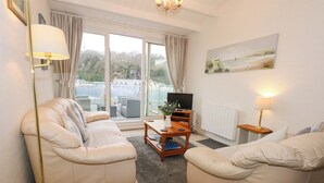 A living room with two beige sofas, a coffee table, a TV, and a painting on the wall. - Anchor Watch (Porthmadog)