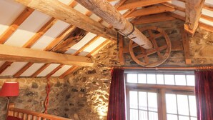 Un intérieur rustique avec des poutres apparentes, un mur en pierre et une grande fenêtre agrémentée de rideaux.
