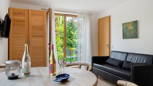Ein Zimmer mit Holztisch, zwei Weinflaschen, einem blauen Teller, einer schwarzen Ledersofa und einem Bild an der Wand.