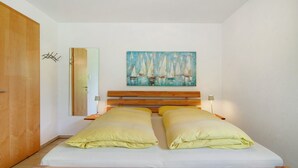 Ein Einzelbett mit Holz Kopfteil, zwei Kissen, ein Nachttisch mit Lampe, ein Segelboothang und ein Spiegel an der Wand.