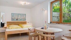 Ein Schlafzimmer mit einem Bett, Holzstühlen, einem runden Tisch, einem Gemälde und einem Fenster mit Blick ins Grüne.