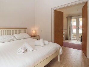 A hotel room with a bed, a nightstand with a lamp, a door leading to a balcony, and a view of the outside. - Newton Calm (Plymouth)