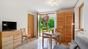A modern living room with a flat-screen TV, wooden furniture, a dining table, and a large sliding glass door leading to a garden. - Apartment 'Marie' with Private Terrace and Wi-Fi (Bodman-Ludwigshafen)