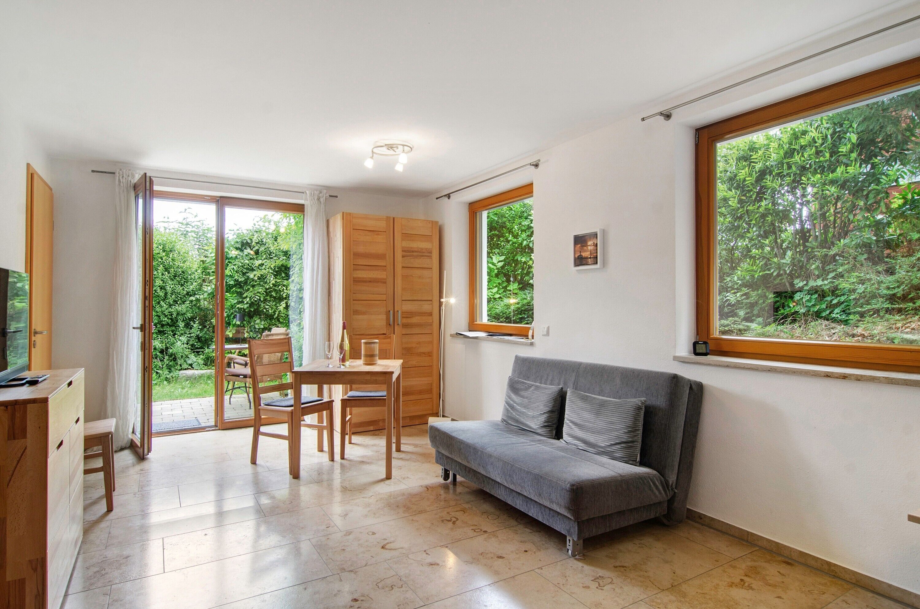 A room with a sofa, a table, chairs, a TV, and a sliding door leading to a garden.