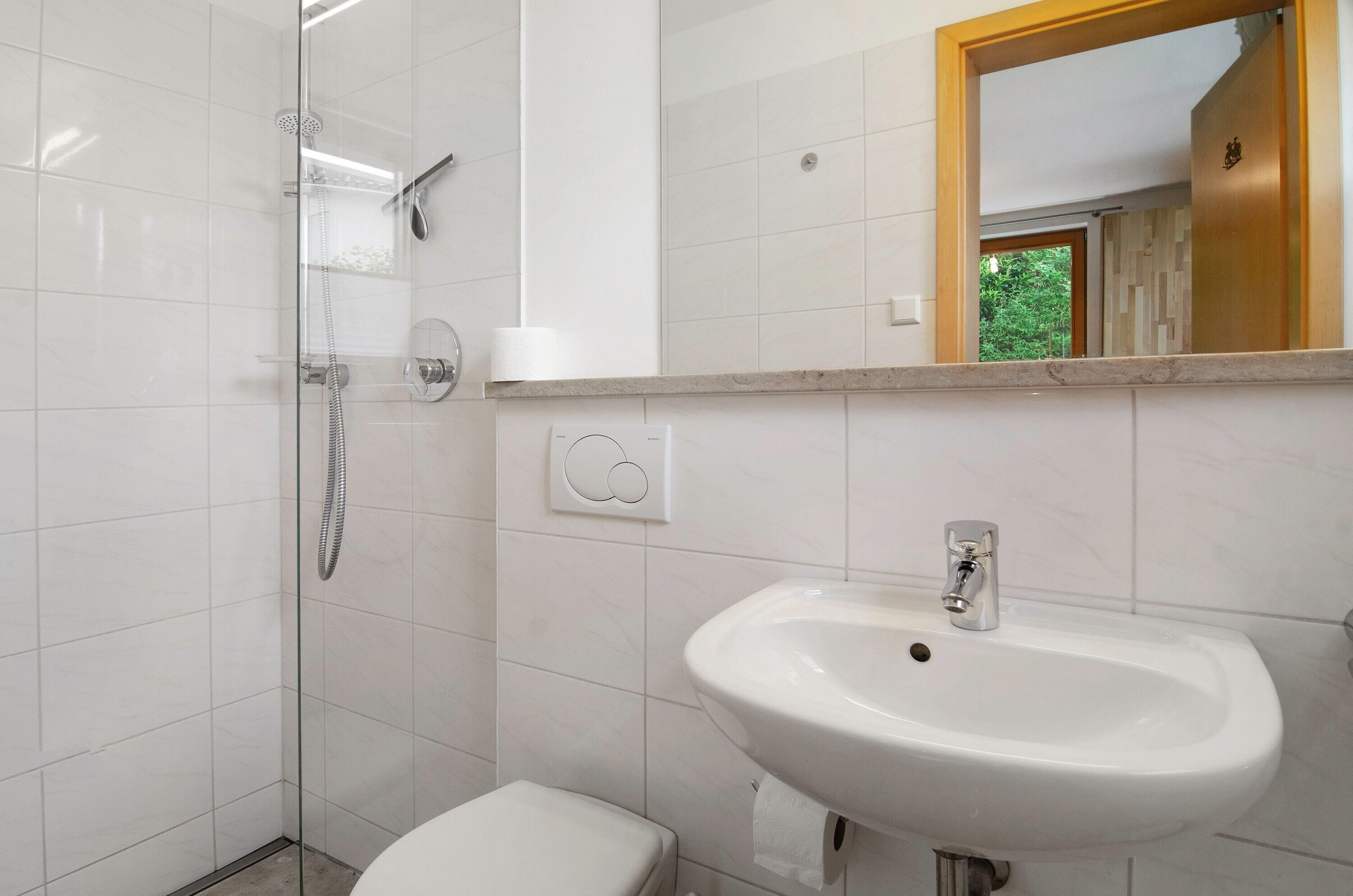 Une salle de bain avec une douche à parois de verre, un lavabo blanc et un miroir avec un cadre en bois.