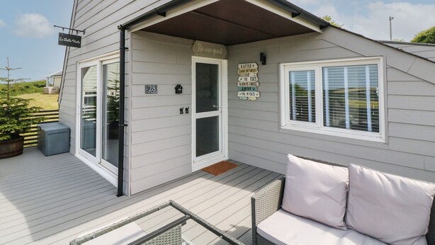 A single-story house with a covered porch, a sliding glass door, and a small outdoor seating area with cushions. - La Bella Vista (Bude)