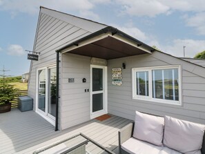 A single-story house with a covered porch, a sliding glass door, and a small outdoor seating area with cushions. - La Bella Vista (Bude)