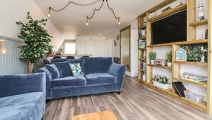 A cozy living room with a blue sofa, wooden shelves, and a wooden coffee table. - La Bella Vista (Bude)