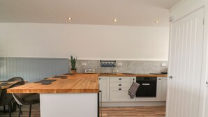 A modern kitchen with a wooden countertop, white cabinets, and a built-in oven. There is a seating area with chairs and a table to the left. - La Bella Vista (Bude)