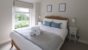 Une chambre avec un grand lit, une fenêtre donnant sur un paysage verdoyant, deux tables de chevet avec des lampes et deux tableaux encadrés accrochés au mur.
