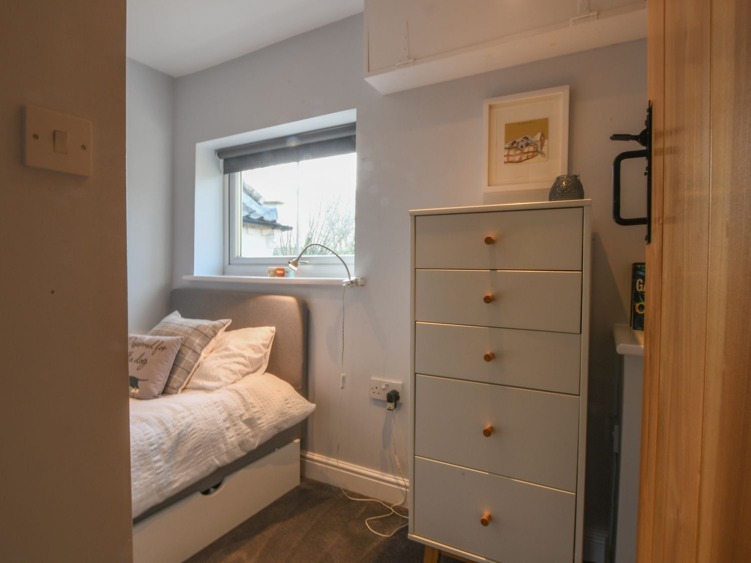 Une petite chambre avec un lit simple, une commode, une fenêtre donnant sur un beau paysage et un luminaire fixé au mur.